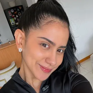 Una mujer con el pelo recogido y chaqueta deportiva negra, sonriendo en la sala de su casa.
