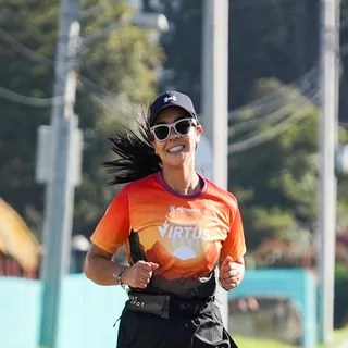 Una mujer corriendo por una calle, con gorra y gafas de sol, sonriendo a la cámara.